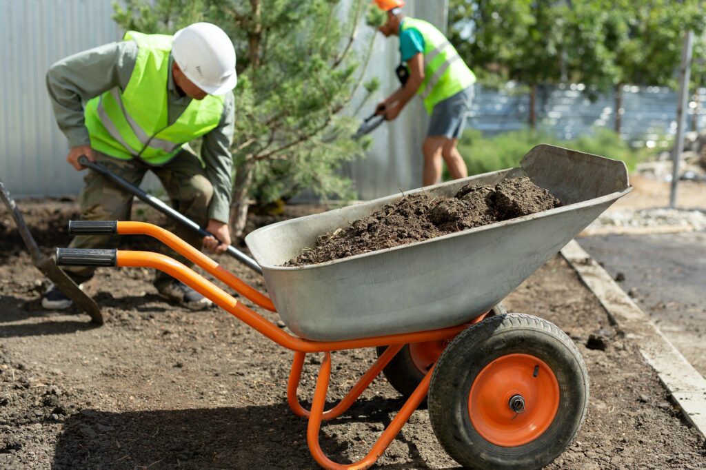 A worker in uniform digs a hole for planting an ornamental tree, loads the earth into a wheelbarrow