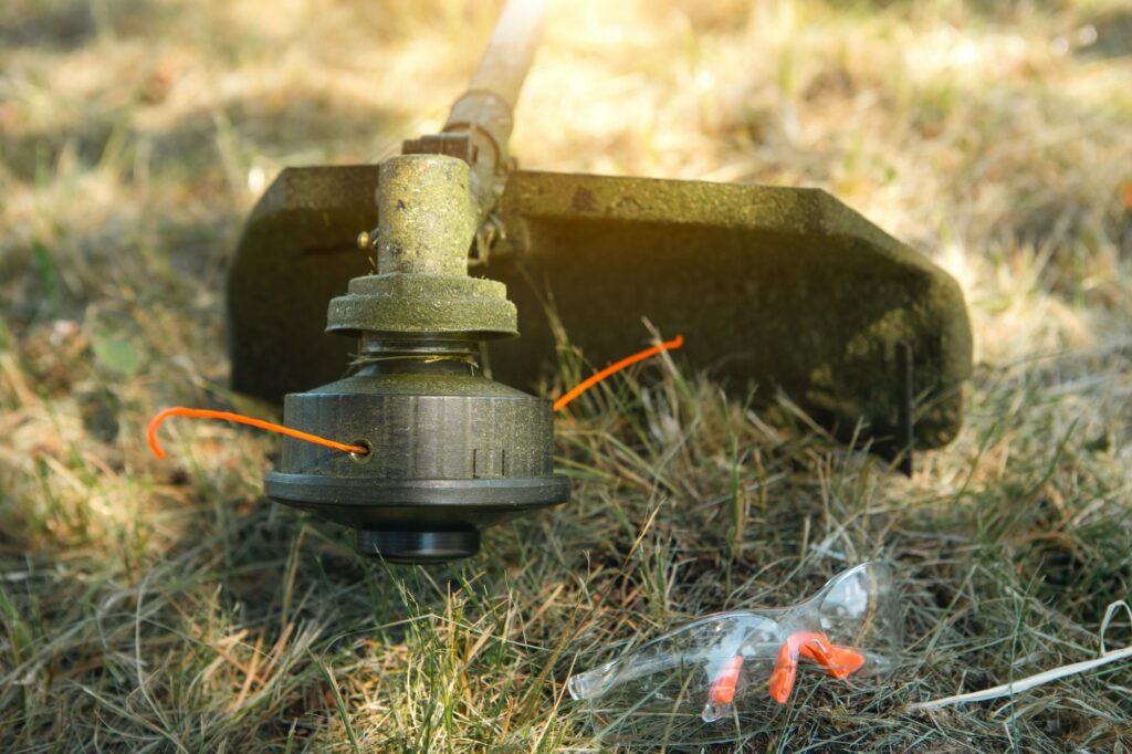 Trimmer after mowing grass close-up. Petrol pump on the grass with safety glasses